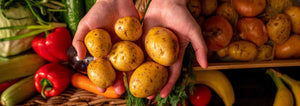 Hands holding fresh potatoes with other vegetables on the table