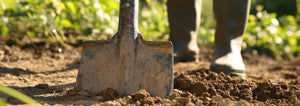 shovel in soil with gardeners boots in background